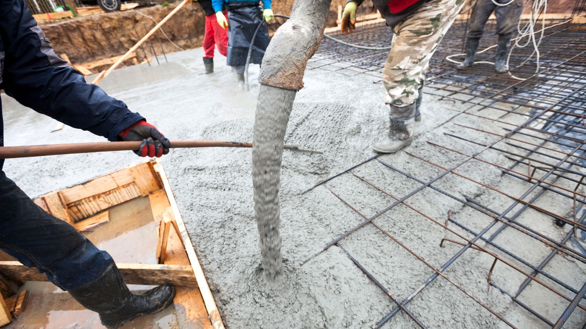 Construction workers pouring concrete over steel reinforcement mesh