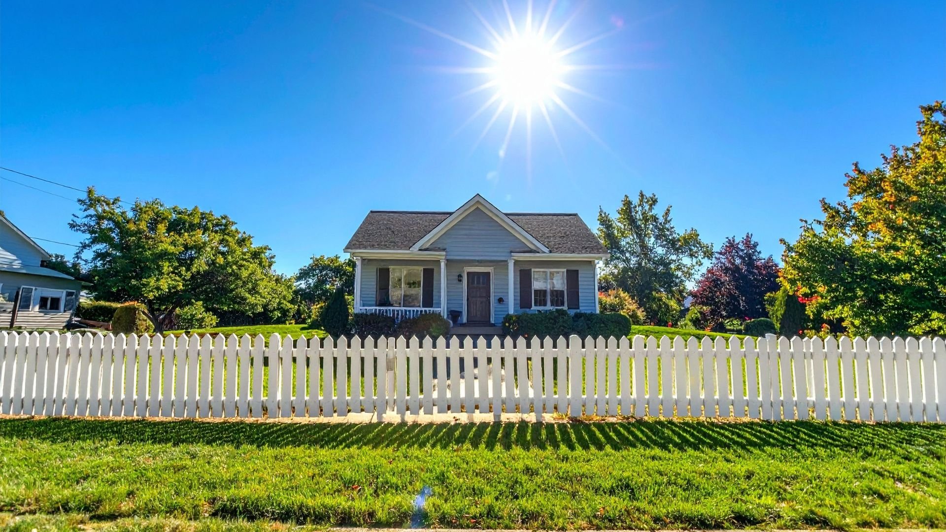 Sunny day with white picket fence and blue house on green lawn