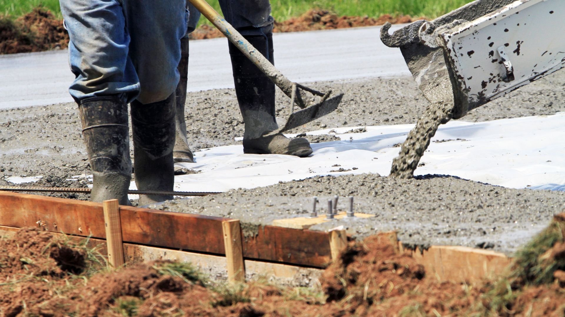 Construction workers pouring and spreading concrete near wooden forms