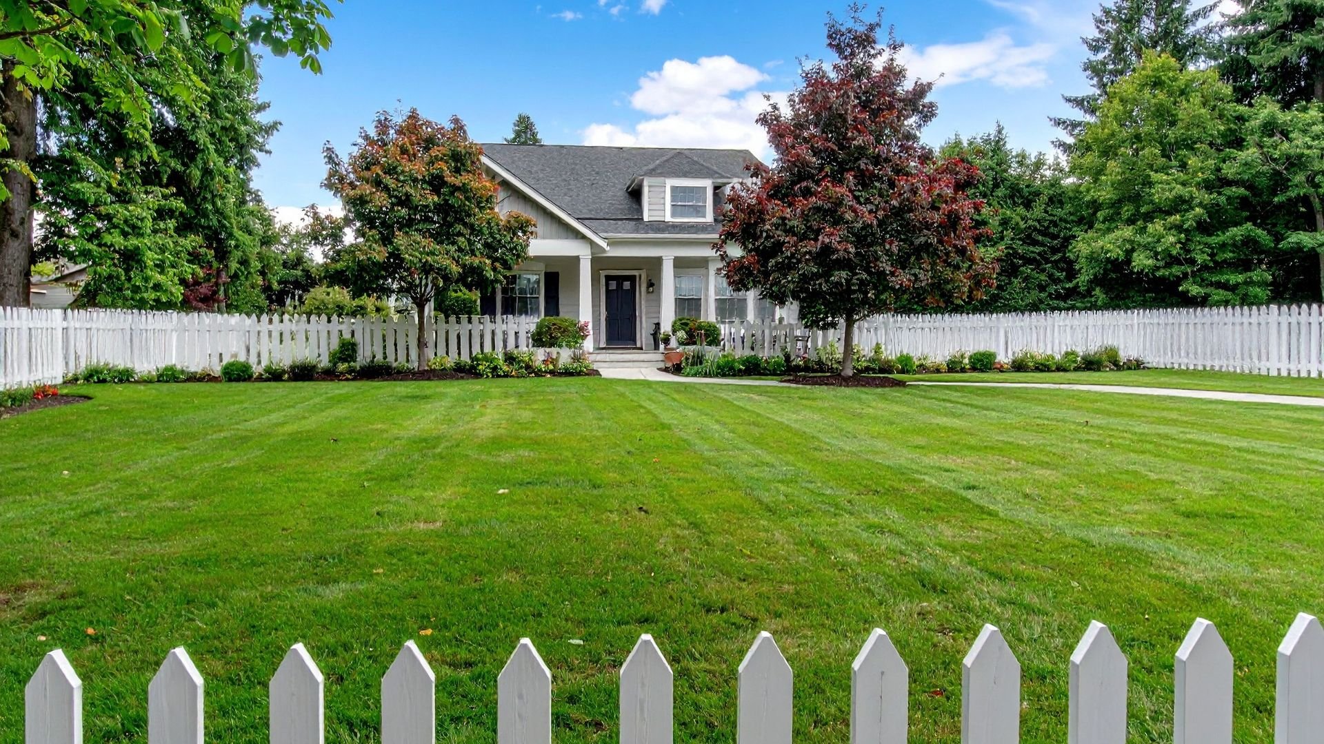 Well-manicured suburban home with white picket fence and lush green lawn